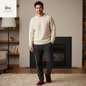 May include: A person wearing a cream-colored sweater and dark gray plaid pants. The person is also wearing burgundy slippers. The background includes a fireplace, bookshelves, and a rug.