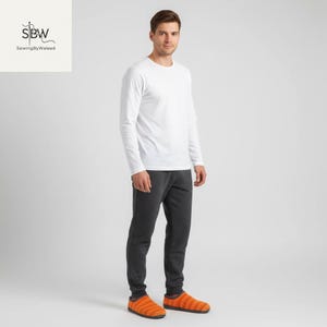 May include: A person wearing a white long-sleeve shirt, dark gray sweatpants, and orange striped slippers. The slippers have a soft, textured appearance. The image is set against a plain white background.