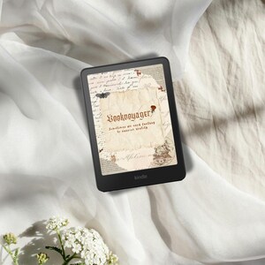 Könnte beinhalten: Schwarzer Kindle-E-Reader mit einer Grafik im Vintage-Stil mit dem Text "Bookvoyager" und dem Zitat "Sometimes we need fantasy to survive reality". Das Gerät liegt auf weißem Stoff, mit weißen Blumen im Vordergrund.