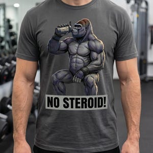 Pode incluir: Camiseta cinza escuro com um gorila musculoso bebendo de uma garrafa de proteína. O gorila está segurando uma garrafa com o rótulo "Gorilla Protein". Abaixo está o texto "NO STEROID!". A camiseta é usada em uma academia.