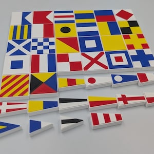 May include: A collection of square and triangular tiles featuring various nautical signal flags in red, white, blue, yellow, and black. The tiles are arranged in a grid pattern with some individual pieces placed separately below the main group.