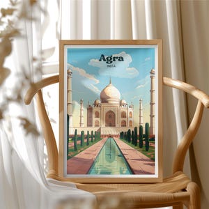 May include: A framed art print featuring the Taj Mahal in Agra, India. The artwork depicts the iconic white marble mausoleum with a reflecting pool and surrounding gardens. The sky is blue with fluffy clouds, and the frame is made of light-colored wood.