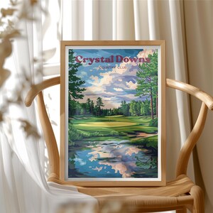 May include: A framed print featuring a golf course scene with the text "Crystal Downs Country Club." The artwork depicts a green golf course with a pond reflecting the sky and clouds. The frame is made of light-colored wood.