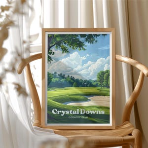 May include: A framed print featuring a golf course scene with a green fairway, sand trap, and a flag. The sky is blue with fluffy white clouds. The print is labeled "Crystal Downs Country Club."