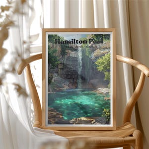 May include: A framed print featuring a scenic view of Hamilton Pool in Texas, United States. The artwork depicts a waterfall cascading into a turquoise pool surrounded by lush greenery and rocky cliffs. The text "Hamilton Pool" is visible at the top.
