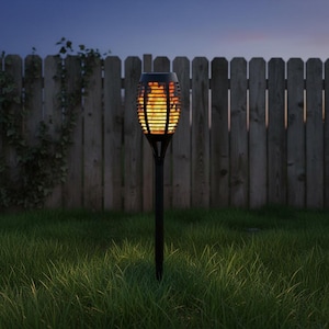 May include: A black solar-powered garden torch with a flickering flame effect. The torch is set in a grassy yard with a wooden fence in the background. The torch is designed to look like a real flame.