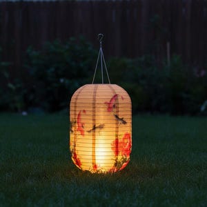 May include: A glowing, paper lantern with a floral and fish design hangs from a wire. The lantern is cylindrical with a curved top and bottom. Red flowers and black fish are visible on the lantern's surface. The lantern is lit from within, casting a warm glow.