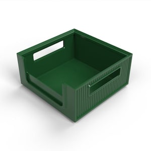 May include: A dark green plastic storage crate with rectangular cut-out handles on the sides. The crate has a square shape with a slightly raised base and vertical ribbed detailing on the exterior.
