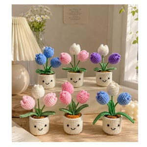 May include: A collection of crocheted tulip plants in small white pots with smiling faces. The tulips are in various colors, including blue, pink, white, and purple. The pots have green leaves and brown soil.