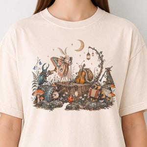T-shirt met insectenmotief in comfortabele kleuren, vintage afbeelding van insectenmuzikanten met een zingende mot, cottagecore bosillustratie.