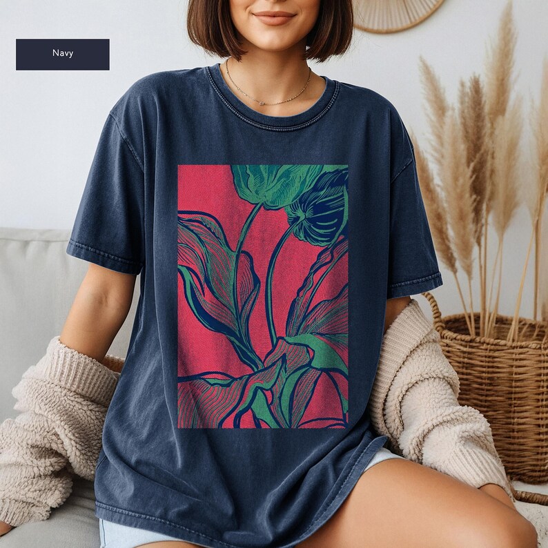 May include: Navy blue t-shirt featuring a vibrant floral design. The graphic showcases green and blue botanical illustrations against a red backdrop. The shirt has a relaxed fit and short sleeves, perfect for casual wear.