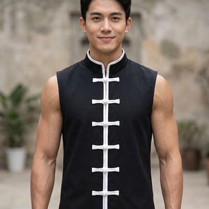 May include: A sleeveless black vest featuring a high mandarin collar and a vertical front placket with white trim. The garment is secured by six white fabric knot buttons arranged in a straight line down the center of the chest.