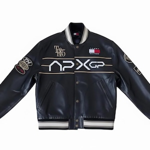 May include: Black leather jacket with white and gold detailing. The front displays the text "185" and "APXGP". Includes patches on the sleeves and the Tommy Hilfiger logo. The jacket has a ribbed collar, cuffs, and hem.