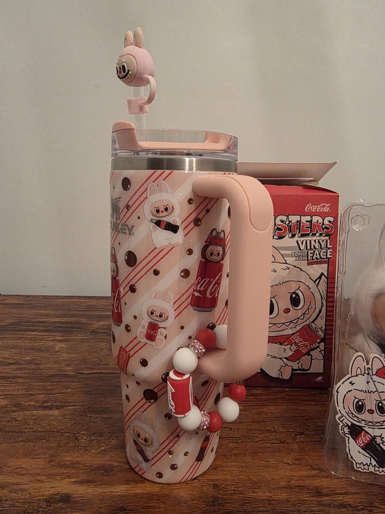 Pu&ograve; includere: Un bicchiere rosa e bianco con manico, con un design a coniglietto dei cartoni animati e il marchio Coca-Cola. Il bicchiere ha un coperchio rosa abbinato e un topper per cannuccia a forma di coniglio. Un braccialetto con ciondoli di perline &egrave; attaccato al manico.