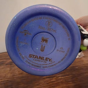 May include: A blue Stanley brand water bottle bottom with the text "30oz / 887mL". The bottle is BPA free and designed in Seattle, WA. The bottle has a metallic finish and the Stanley logo.