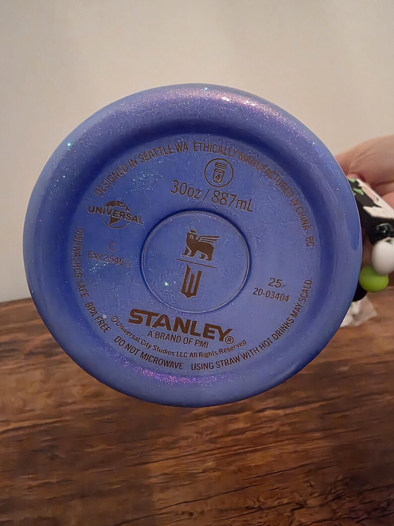 May include: A blue Stanley brand water bottle bottom with the text "30oz / 887mL". The bottle is BPA free and designed in Seattle, WA. The bottle has a metallic finish and the Stanley logo.