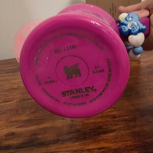 May include: A bright pink Stanley brand water bottle, with the bottom of the bottle facing the camera. The bottle is labeled as 40oz / 1.18L. The text "Dishwasher Safe" and "Do Not Microwave" are also visible.