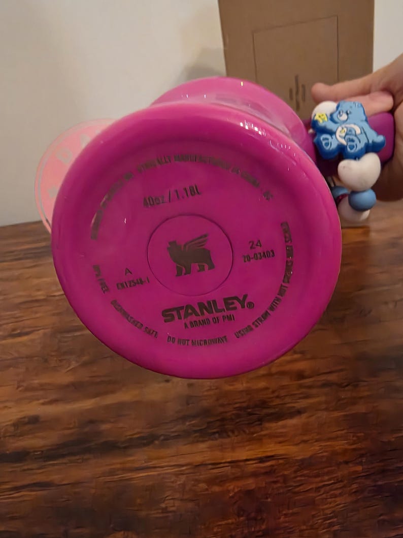 May include: A bright pink Stanley brand water bottle, with the bottom of the bottle facing the camera. The bottle is labeled as 40oz / 1.18L. The text "Dishwasher Safe" and "Do Not Microwave" are also visible.