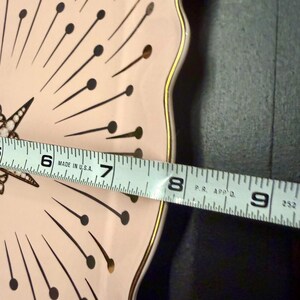 Op de afbeelding: Een lichtroze bord met geschulpte rand, een gouden rand en een zwart-goudkleurig sterrenpatroon. De diameter van het bord is ongeveer 20 cm. De tekst "MADE IN U.S.A." is zichtbaar.