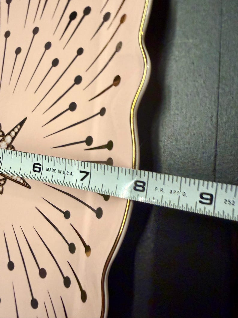Op de afbeelding: Een lichtroze bord met geschulpte rand, een gouden rand en een zwart-goudkleurig sterrenpatroon. De diameter van het bord is ongeveer 20 cm. De tekst "MADE IN U.S.A." is zichtbaar.