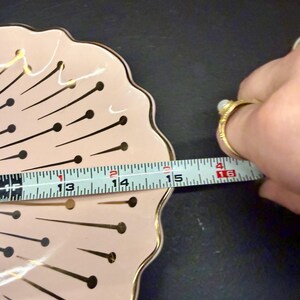 Op de afbeelding: Een roze decoratieve schaal met een geschulpte rand en gouden rand. De schaal heeft een patroon van zwarte lijnen met gouden stippen. De diameter van de schaal is ongeveer 35,5 cm.