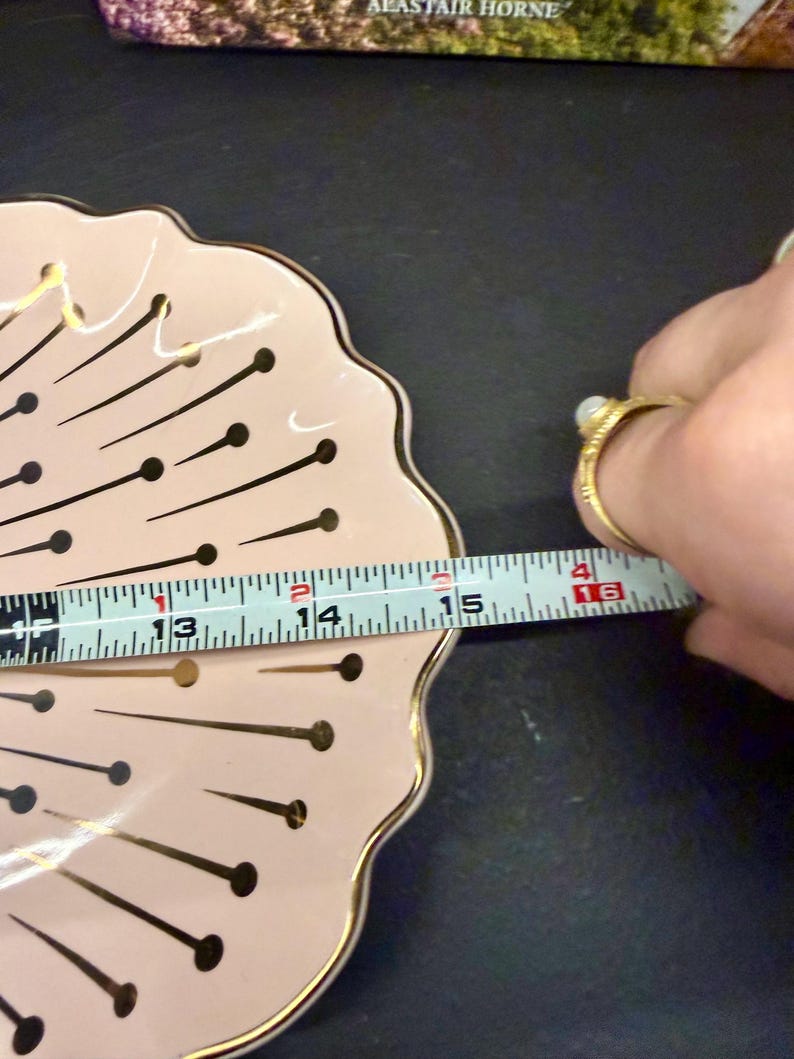 Op de afbeelding: Een roze decoratieve schaal met een geschulpte rand en gouden rand. De schaal heeft een patroon van zwarte lijnen met gouden stippen. De diameter van de schaal is ongeveer 35,5 cm.