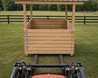 Puede incluir: Un comedero de madera con listones horizontales y un techo de metal corrugado, colocado sobre las horquillas de un tractor naranja. La estructura cuenta con bisagras de metal plateado en los paneles laterales y un diseño abierto.