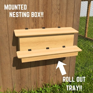 Może przedstawiać: Jasnobrązowa drewniana budka lęgowa montowana na ścianie z uchylną pokrywą i wysuwaną tacą na dole. Tekst MOUNTED NESTING BOX!! jest widoczny w lewym górnym rogu, a tekst ROLL OUT TRAY!! ze strzałką znajduje się w prawym dolnym rogu.