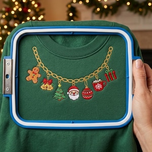 May include: A dark green sweatshirt secured in a blue and white embroidery hoop. The fabric features an embroidered gold chain necklace design with hanging Christmas charms including a gingerbread man, bells, tree, Santa, ornament, mug, and gift.