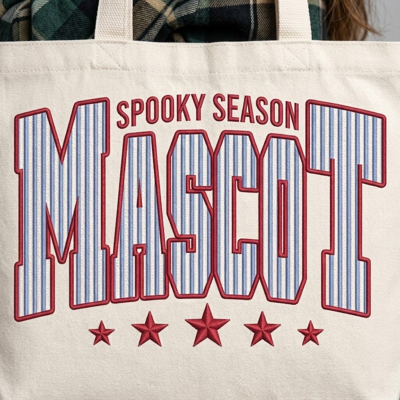 May include: A cream-colored canvas tote bag featuring the text SPOOKY SEASON MASCOT in large, block-style letters with a blue and white pinstripe pattern and red outlines. Below the text are five red embroidered stars arranged in a horizontal row.