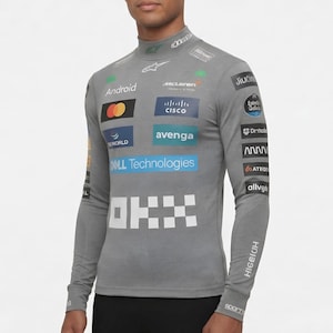 Może przedstawiać: Szara koszulka z długim rękawem i stójką, z logo sponsorów i logo McLaren. Koszulka ma logo Android, Cisco, Dell Technologies i OKX. Na rękawach widnieją napisy "HIGEIOH" i "SPORT".