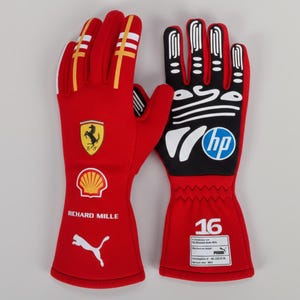 Puede incluir: Par de guantes de carreras rojos con detalles amarillos y blancos. Presentan el logotipo de Ferrari, el logotipo de Shell y el logotipo de Puma. Los guantes tambi&eacute;n tienen el texto "RICHARD MILLE" y el logotipo "hp".