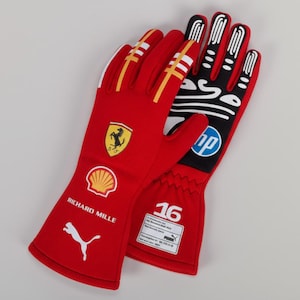 Puede incluir: Un par de guantes de carreras rojos con detalles blancos y amarillos. Los guantes presentan el logotipo de Ferrari, el logotipo de Shell, el logotipo de Puma y el texto "Richard Mille". El guante derecho tiene el logotipo de HP y el n&uacute;mero "16".