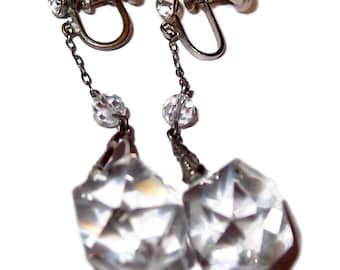 Könnte beinhalten: Ein Paar silberfarbene Ohrclips mit einem baumelnden Kristalltropfen. Die Ohrringe haben eine Kette mit einer kleinen Kristallperle und einem größeren facettierten Kristalltropfen.