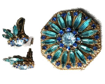 May include: A vintage brooch and earrings set featuring a large octagonal brooch with a blue and turquoise rhinestone design. The brooch has a central light blue rhinestone surrounded by smaller blue rhinestones and turquoise leaves.