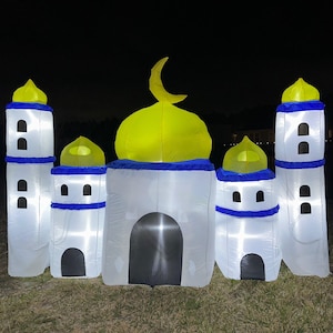 May include: An inflatable mosque with a yellow dome and crescent moon, white walls, and blue accents. The structure has multiple towers and is illuminated with internal lights, set against a dark night sky.