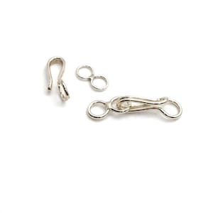 May include: Three silver-colored jewelry clasps are displayed against a white background. The clasps include a hook, a figure-eight connector, and a clasp with a hook and eye closure. These components are used for necklaces and bracelets.