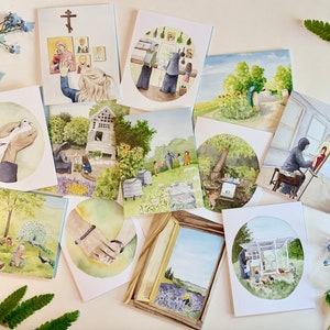 May include: A set of ten watercolor greeting cards featuring various scenes, including a garden, a church, a dove, and a woman painting. The cards are all white with a light blue border.
