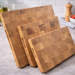 May include: Three wooden butcher block cutting boards of varying sizes. The boards are made of light brown wood and have a rectangular shape with a handle cutout. The boards are arranged in a staggered fashion, showcasing their different sizes.