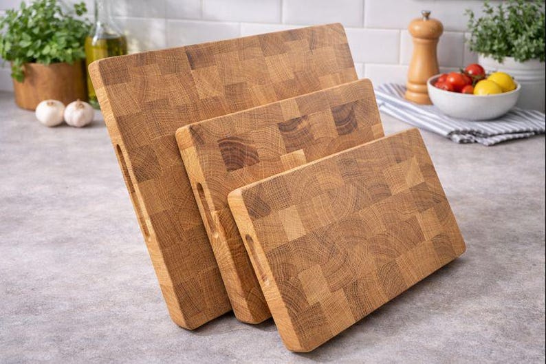 May include: Three wooden butcher block cutting boards of varying sizes. The boards are made of light brown wood and have a rectangular shape with a handle cutout. The boards are arranged in a staggered fashion, showcasing their different sizes.