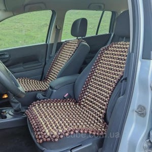 Op de afbeelding: Twee auto stoelhoezen gemaakt van houten kralen. De kralen zijn een mix van licht- en donkerbruin, gerangschikt in een patroon. De hoezen zijn geplaatst op de voorstoelen van een auto, met de hoofdsteunen ook bedekt.