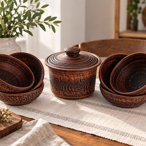 Pode incluir: Um conjunto de cerâmica de argila castanho-escura composto por uma taça com tampa e quatro taças a condizer. Cada peça apresenta uma superfície texturada com padrões florais em relevo e um acabamento polido num tom castanho-avermelhado.
