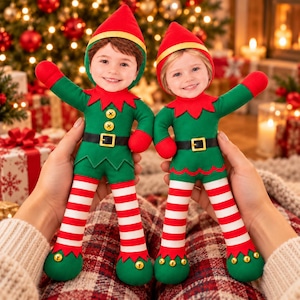 May include: Two plush elf dolls featuring custom photo faces, wearing green tunics with yellow buttons, black belts with gold buckles, red and white striped leggings, and red pointed hats with gold trim. Each doll has green pointed shoes with gold bells.