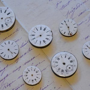 May include: Seven antique pocket watches with white faces and black Roman numeral markings. The watches are arranged on a white surface with handwritten text.
