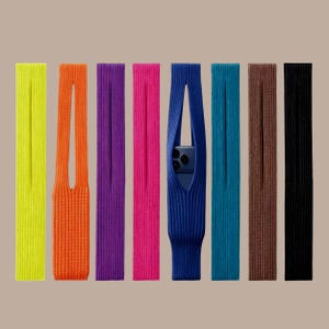 May include: A collection of colorful knitted phone cases in various shades, including yellow, orange, purple, pink, blue, teal, brown, and black. One case holds a blue smartphone, showcasing the product's functionality and design.