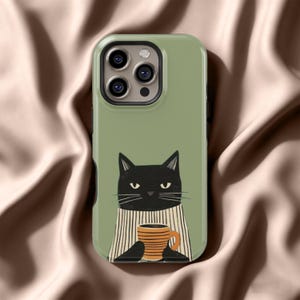 以下が含まれることがあります： セージグリーンの携帯電話ケース。黒猫のイラストが描かれており、縞模様のオレンジ色のマグカップを持っています。猫は縞模様のスカーフを着用しています。ケースにはカメラの切り抜きがあり、光沢のある仕上がりです。