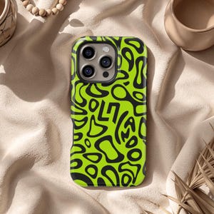 以下が含まれることがあります： 黒い抽象的なデザインのネオングリーンの携帯電話ケース。ケースは光沢のある仕上がりで、カメラレンズの周りに隆起したエッジがあります。デザインは有機的な形と線で構成されています。