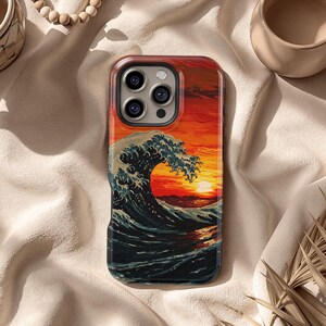 May include: A phone case featuring a vibrant print of a large ocean wave under a sunset. The design showcases a dynamic wave with white crests against a backdrop of orange and red hues. The case has a glossy finish.