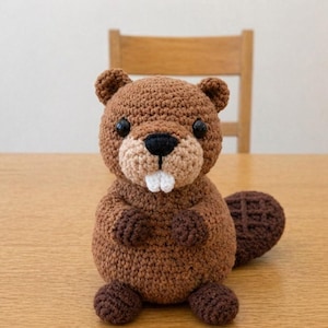 May include: A handmade brown crochet beaver doll with a light brown snout, white teeth, and a dark brown tail. The beaver has black eyes and small arms and feet. The doll is sitting on a wooden table.