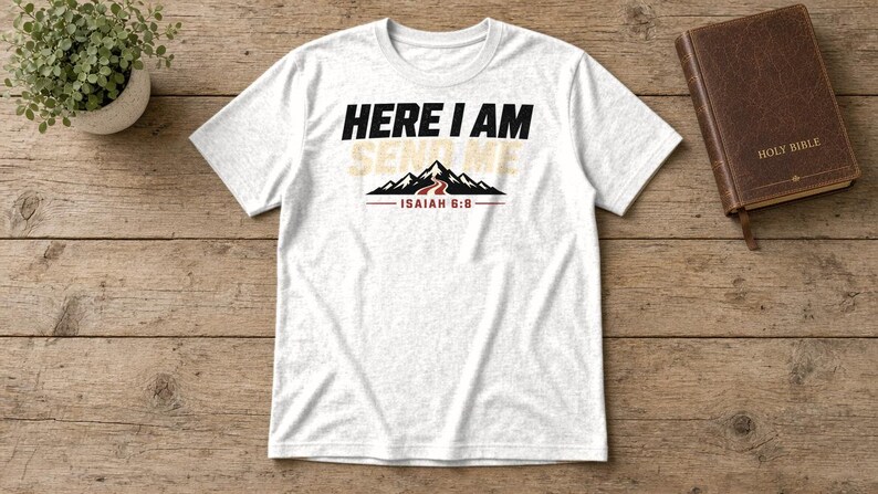 Pu&ograve; includere: Una t-shirt bianca a maniche corte con il testo nero HERE I AM, il testo beige SEND ME e un grafico di montagne nere con un sentiero rosso. Sotto il grafico della montagna c'&egrave; il testo rosso ISAIAH 6:8 con una linea rossa su ogni lato.